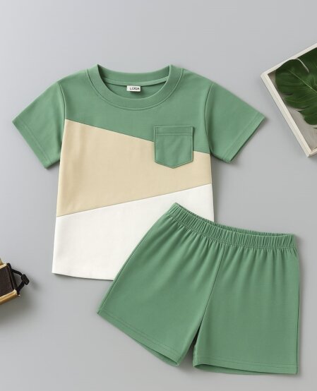 Completo estivo bambino disposto su sfondo neutro: maglietta a maniche corte con pannelli verde, beige e bianco e taschino sul petto, abbinata a pantaloncini verdi.<br /><br /><br /><br /><br /><br /><br /><br /><br /><br />