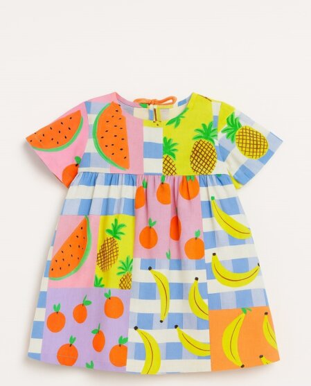 Vestito estivo per bambina con maniche corte e taglio svasato, decorato con una vivace stampa a riquadri multicolore raffigurante frutti come angurie, banane, ananas e arance su sfondi a quadretti bianchi e blu, rosa, lilla e giallo lime. Presenta un laccetto sul retro per la chiusura.