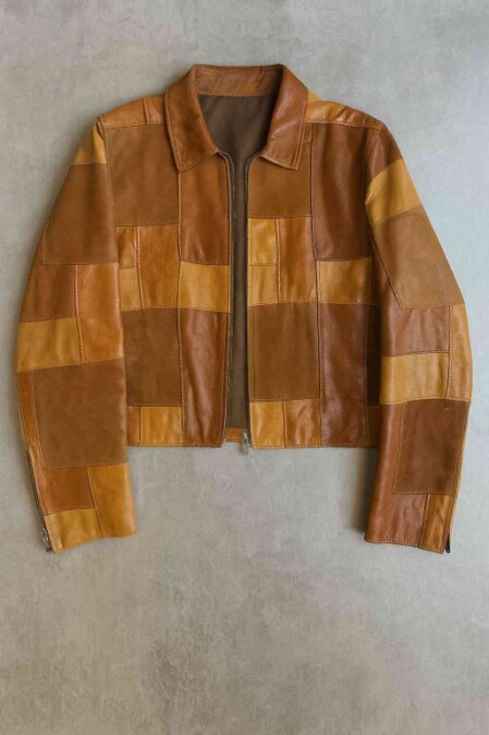 Giacca in pelle patchwork con pannelli nei toni del marrone, cognac e beige, dal taglio squadrato e vintage su sfondo grigio.