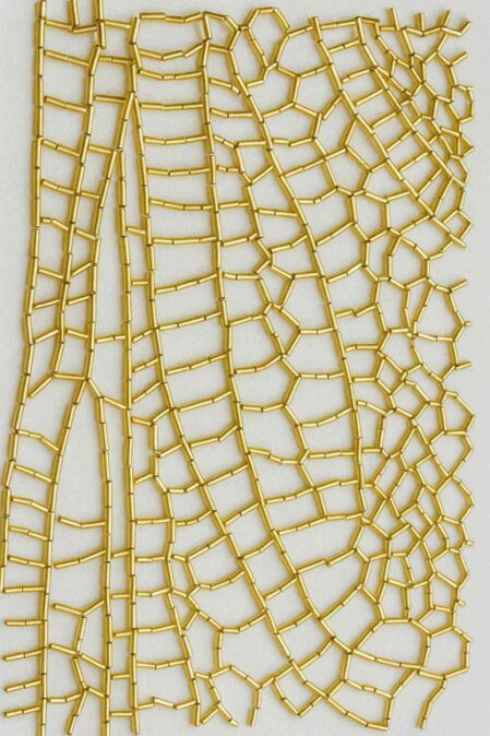 Struttura geometrica irregolare realizzata con perline dorate cucite su tessuto bianco, simile a una ragnatela.