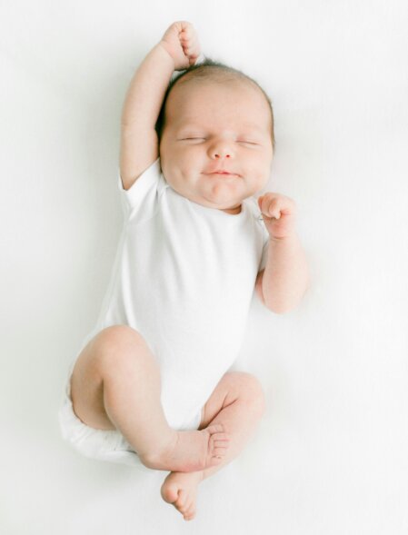 Neonato che dorme indossando un body bianco minimal, su sfondo chiaro ideale per collezione abbigliamento baby essenziale e confortevole.